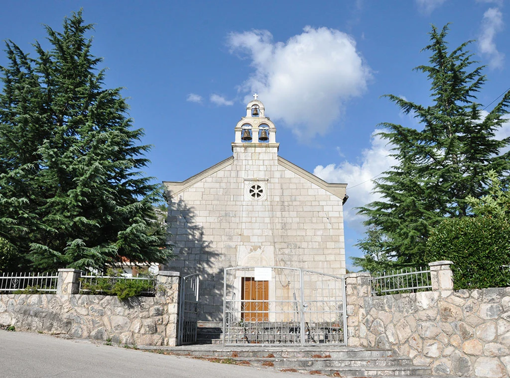 A woman wearing glasses, a white blouse, and a tan corduroy blazer sits at a table with her hands clasped during a professional meeting
